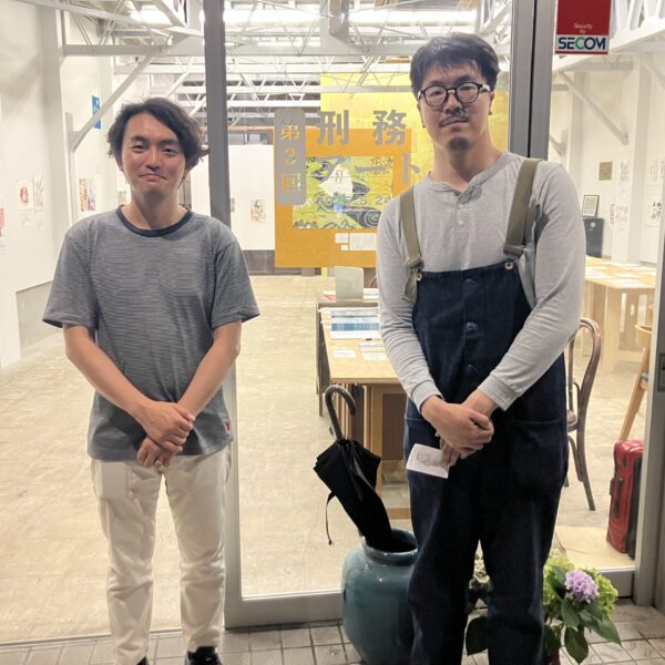 Prison Arts Connections共同代表理事の鈴木悠平（写真左）と風間勇助（写真右）が展示会場入口で立っている写真