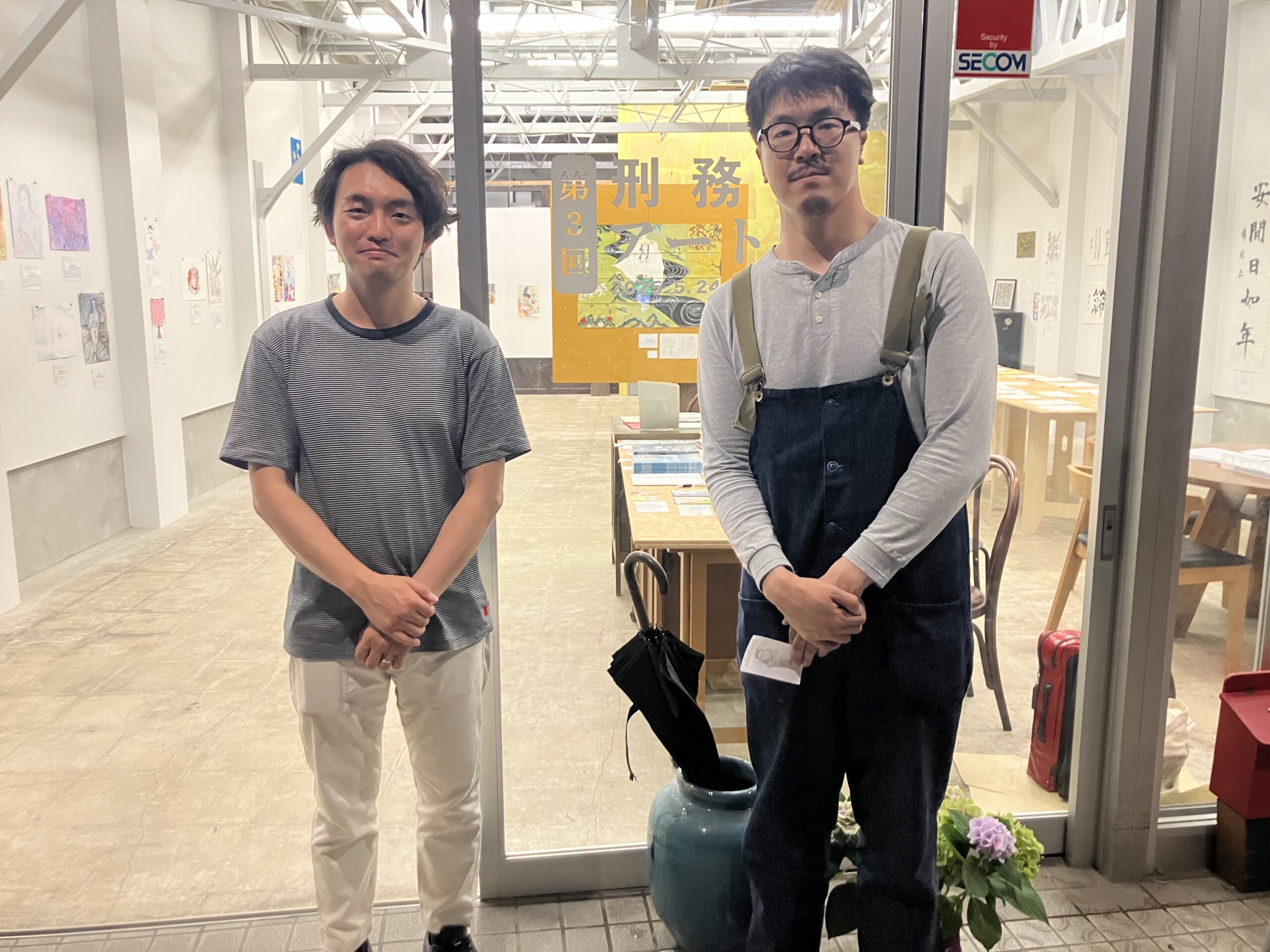 Prison Arts Connections共同代表理事の鈴木悠平(写真左)と風間勇助(写真右)が展示会場入口で立っている写真