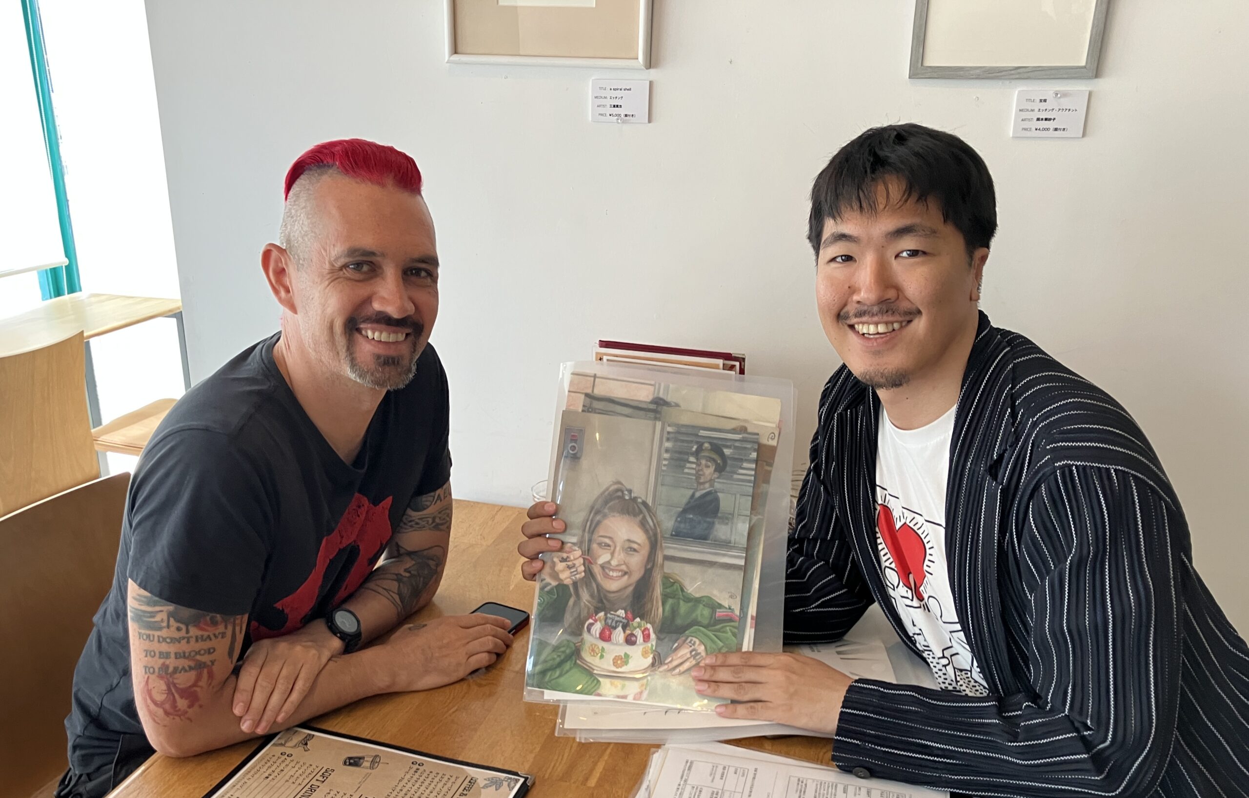左側にいるのが『Paper Chained』の編集長、ダミアン・リネンさん。右側にはPAC共同代表の風間が謎の画家Dさんの作品を手にしている。