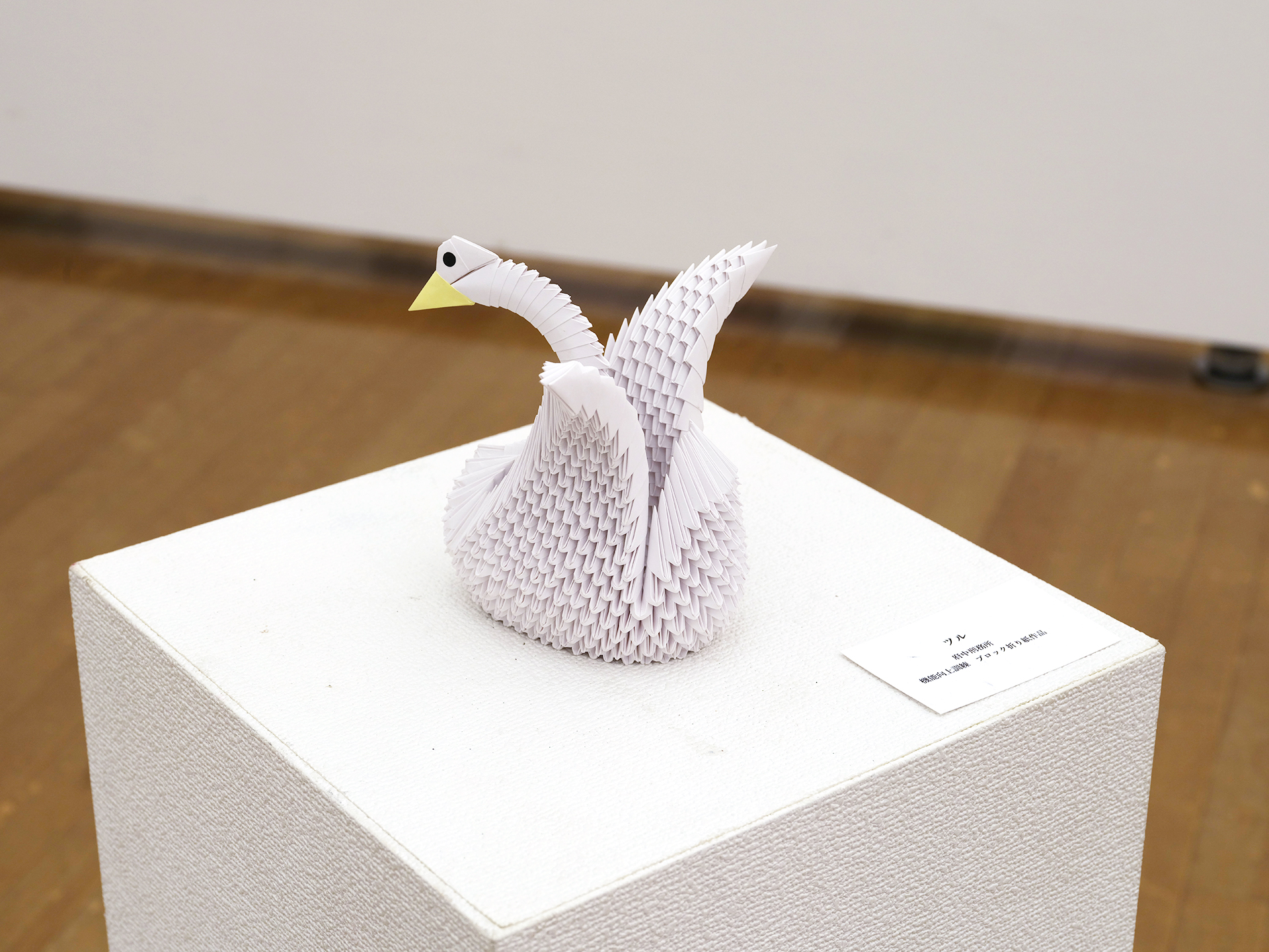 白（淡い藤色）の小さな三角パーツを多数組み上げた立体折り紙。長い首をゆるやかにもたげ、黄色いくちばしと黒い目をもつ白鳥のような鳥を表す。左右に翼を広げている。