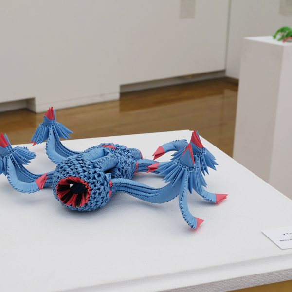 青色の三角パーツで組み上げた多脚の海の怪物（クラーケン）風の立体折り紙。波打つ複数の触手をもち、先端やところどころに赤い差し色。中央に赤く縁どられた口のような開口部がある。
