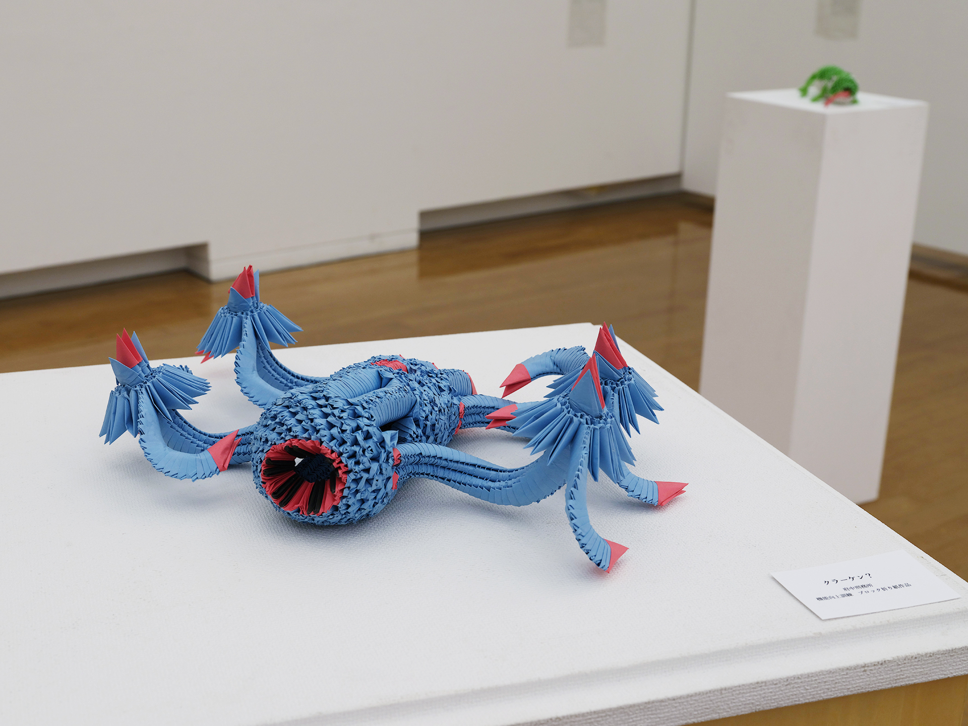 青色の三角パーツで組み上げた多脚の海の怪物（クラーケン）風の立体折り紙。波打つ複数の触手をもち、先端やところどころに赤い差し色。中央に赤く縁どられた口のような開口部がある。