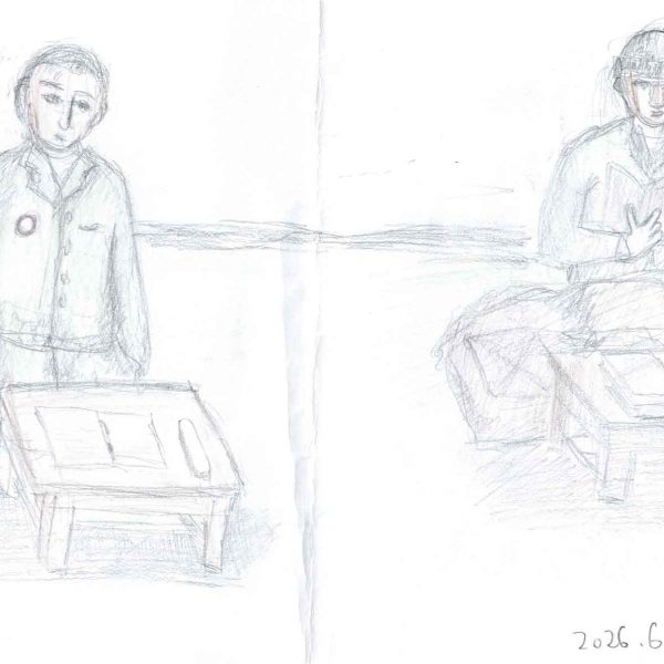 鉛筆と色鉛筆による線画。横長の紙の左右に、灰色の上着の人物が一人ずつ、低い木の机の前に座って正面を向く。左の人物は胸に赤い縁の丸いバッジを付け、机上に開いた冊子。右の人物は帽子をかぶり、両手で開いた本を持ち、膝の前に布団のような膨らみがあり、机上にも本と細長い物が置かれる。背景に水平の線が一本。右下に「2026.6.28」の書き込み。紙の中央に縦の折り目。