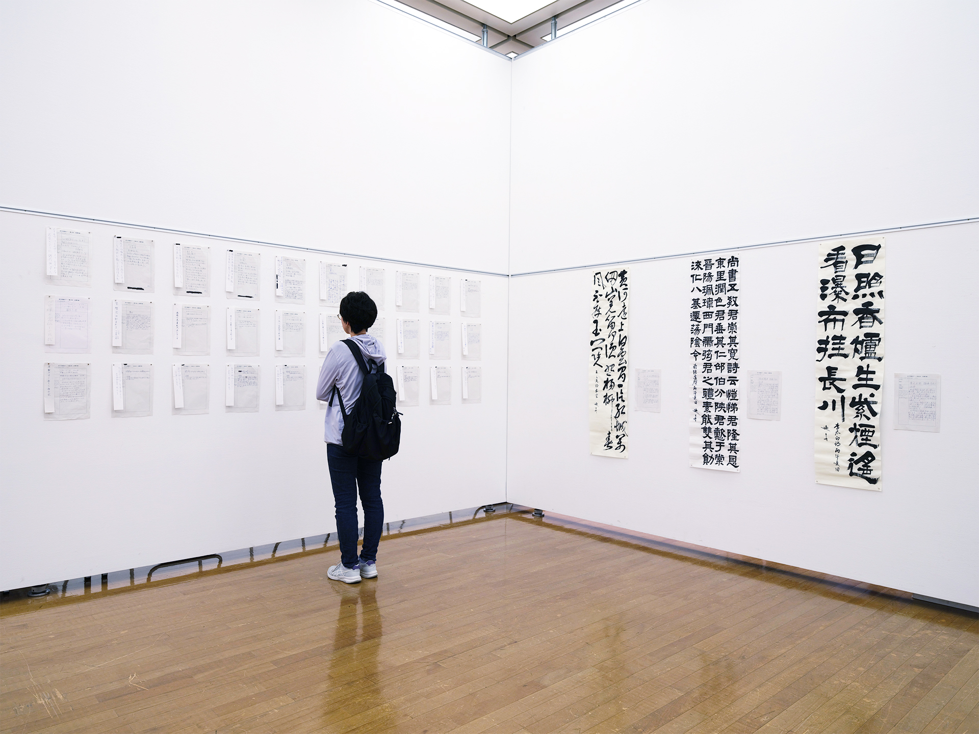 第1部の展示風景。俳句・短歌の書が並ぶコーナーと、来場者が書の掛軸作品を見つめる様子