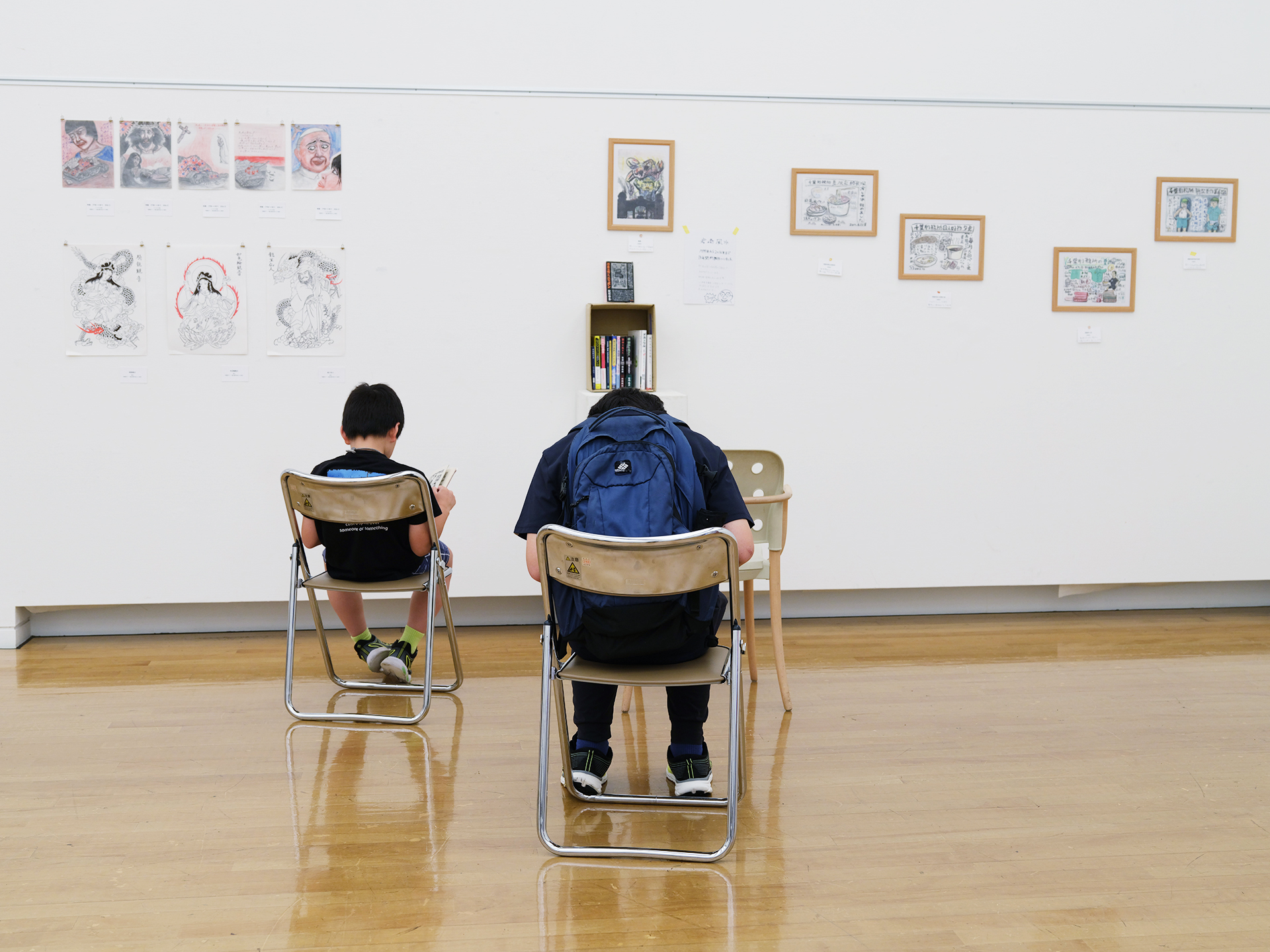 第3部の展示風景。刑務所内の日常を描いた作品を、親子連れが座って鑑賞している様子